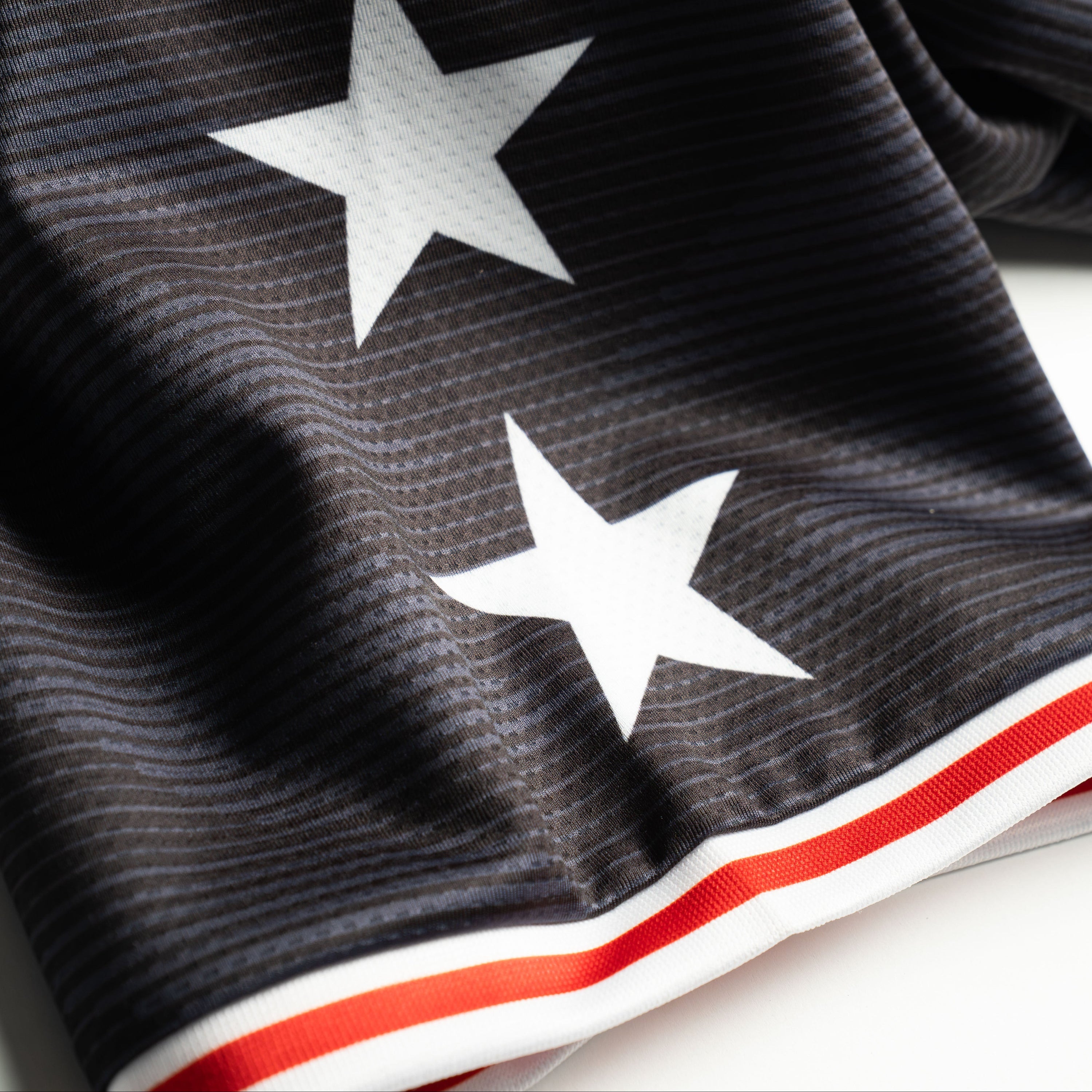 Close-up of a black athletic jersey with a white star pattern and a red and white striped trim.