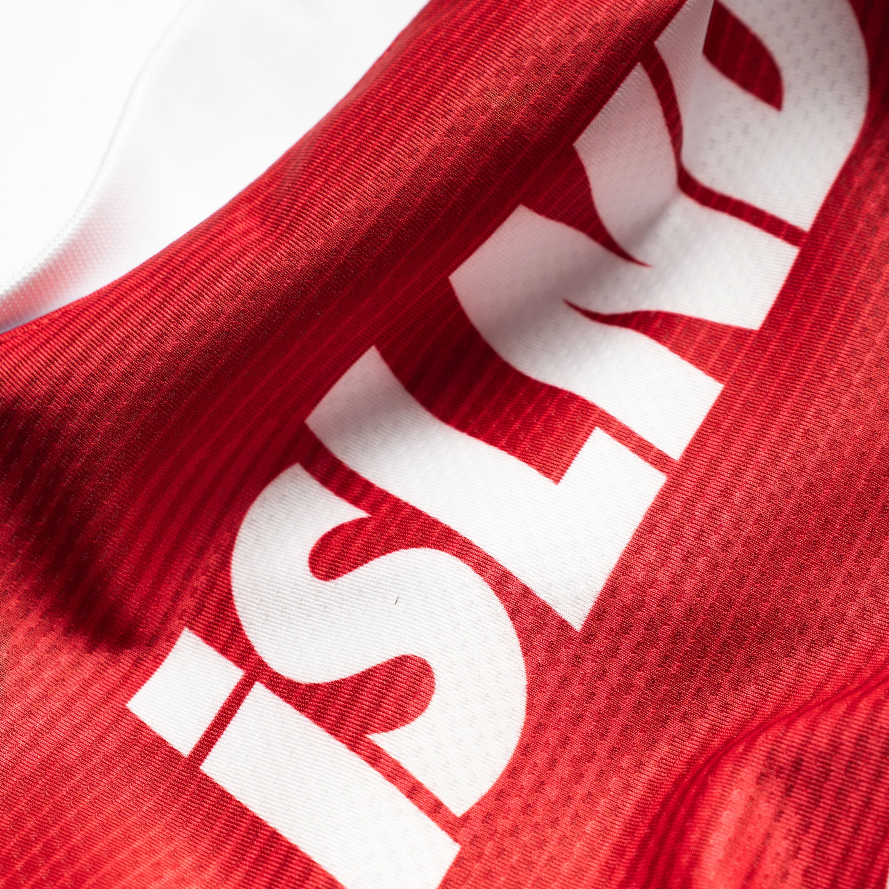 Close-up of a red athletic jersey with a large white 'ISLAND' graphic printed diagonally across the fabric.